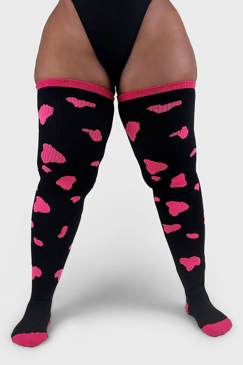 A pair of thigh-high socks with a cow print pattern featuring black fabric and neon pink spots.