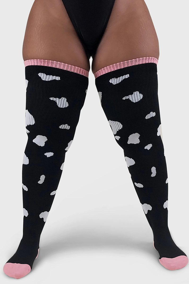 A pair of thigh-high socks with a cow print pattern, predominantly black with white spots, and pink at the cuffs.