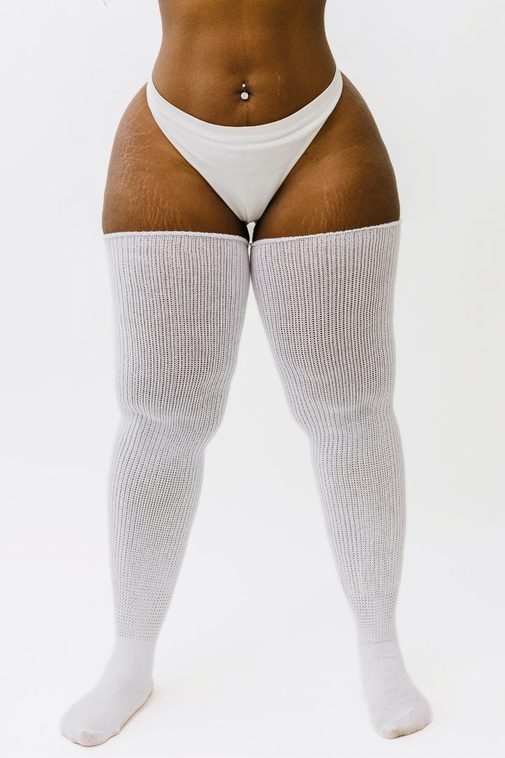 A pair of milky white thigh-high socks, displayed on a model. The socks are designed to fit over the upper legs and have a ribbed texture.